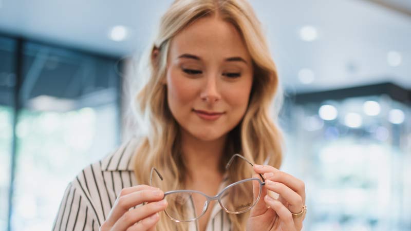 Young woman holding a pair of designer frames in Korrect Optical showroom in Louisville, Kentucky.